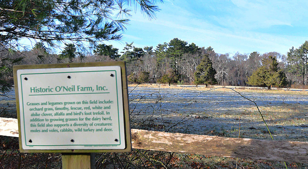 A photograph of a property sign with a farm field in the background.