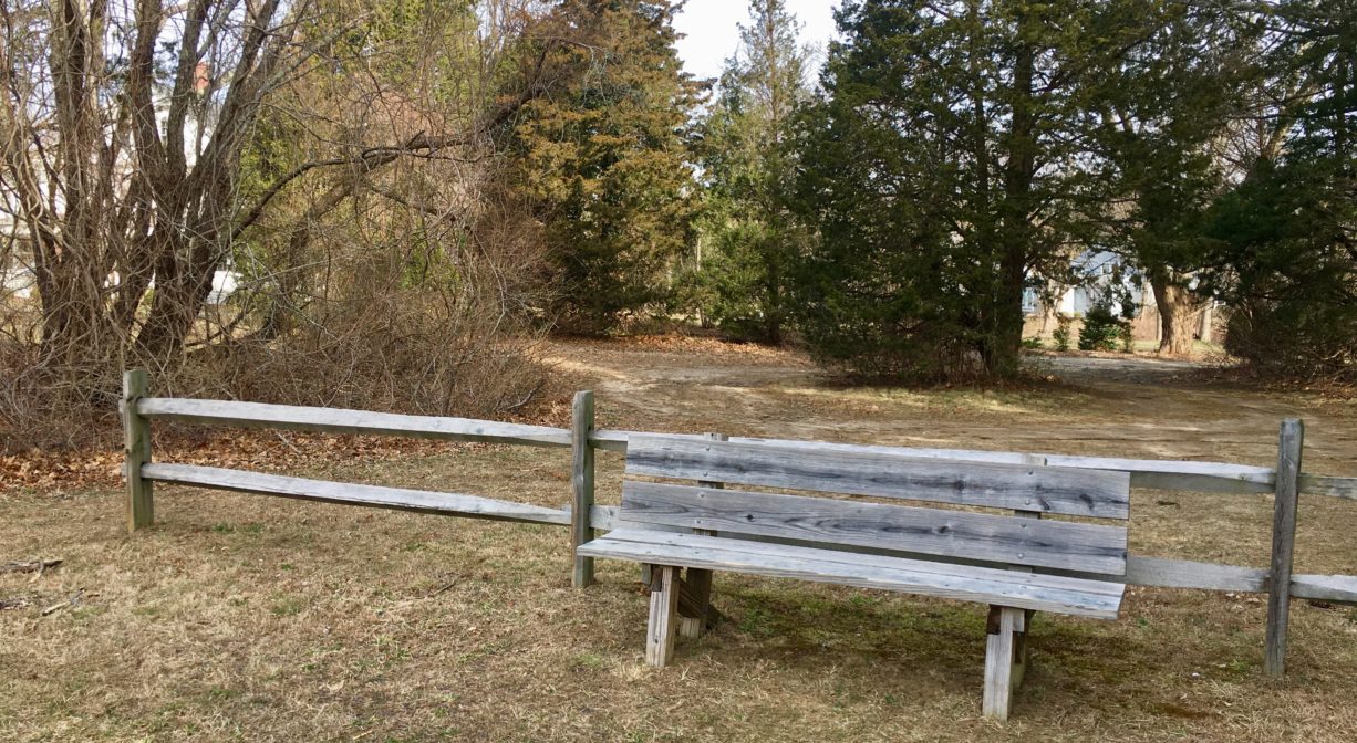 A photograph of a bench beside a fence in a grassy area.