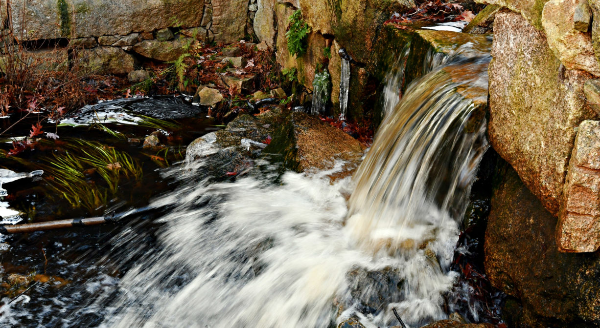 A photograph of a stream flowing through a granite dam.