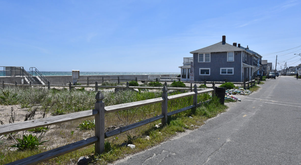 A photograph of a grassy beachfront area with a fence.