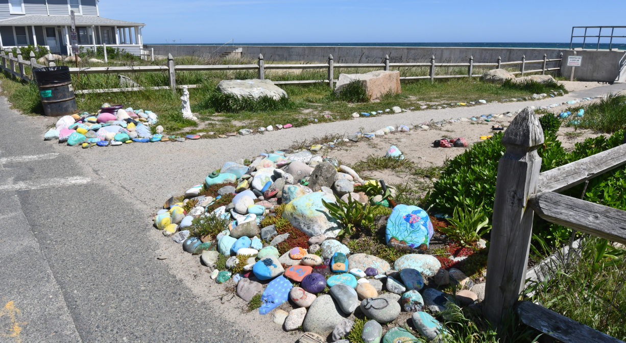 A photograph of a pedestrian entrance to a beach with numerous painted stones.