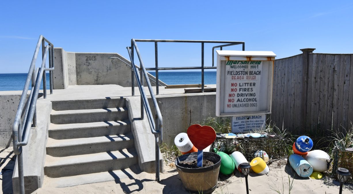 A photograph of a staircase on a seawall, with a property sign and colorful buoys to one side.