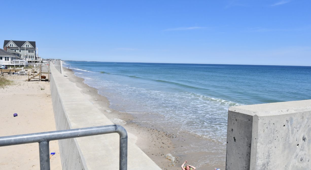 A photograph of a beach with a long sea wall.