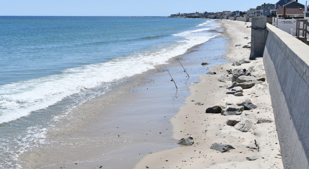 A photograph of an ocean beach with a long sea wall.