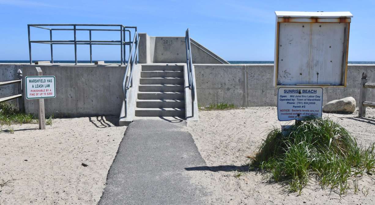 A photograph of a paved path leading to a concrete staircase on a seawall.