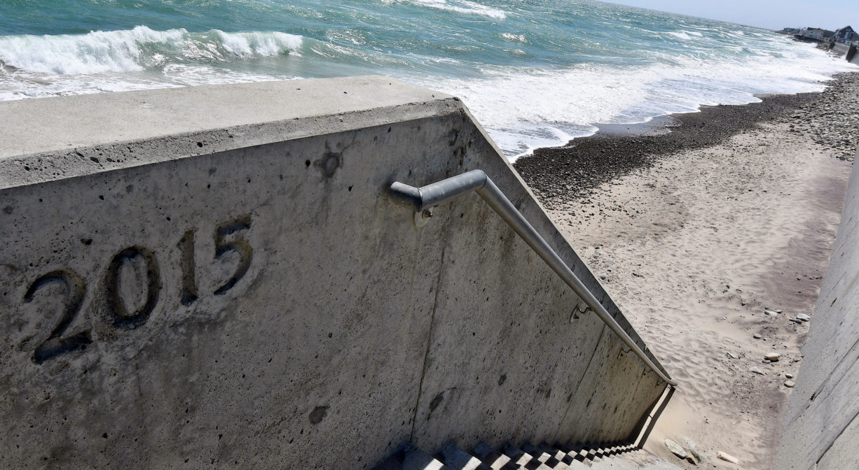 A photograph of a concrete staircase leading down to a sandy ocean beach.