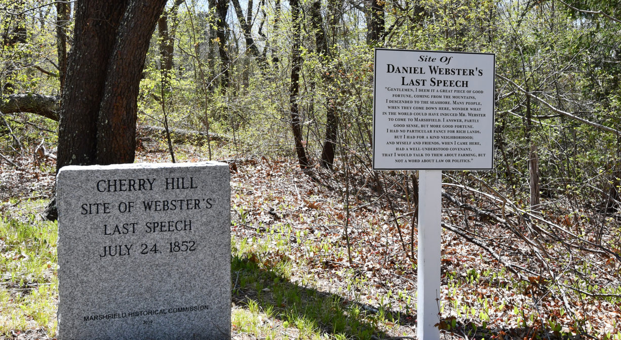 A photograph of two historic markers with grass and trees.