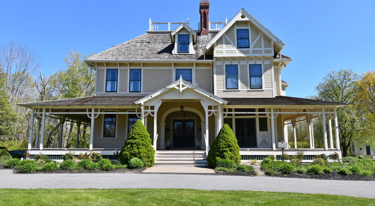 A photograph of a historic estate with a driveway and lawn in the foreground.