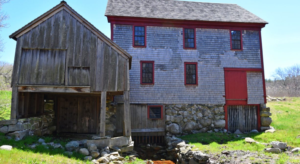 A photograph of a mill building and a stream, viewed from the back.