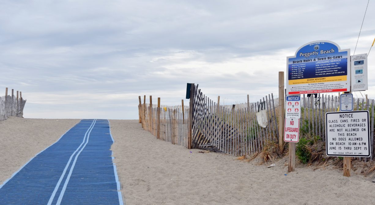 A photograph of a beach entrance with a blue access mat and signage.