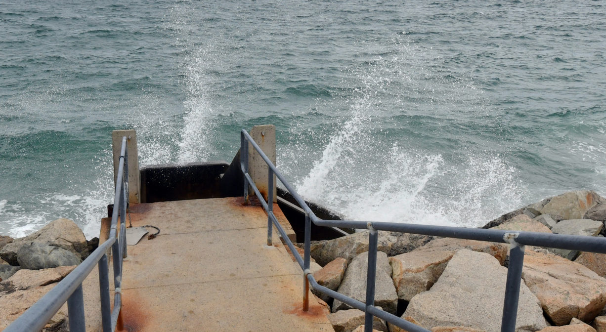 A photograph of a stairway leading to a rocky beach.