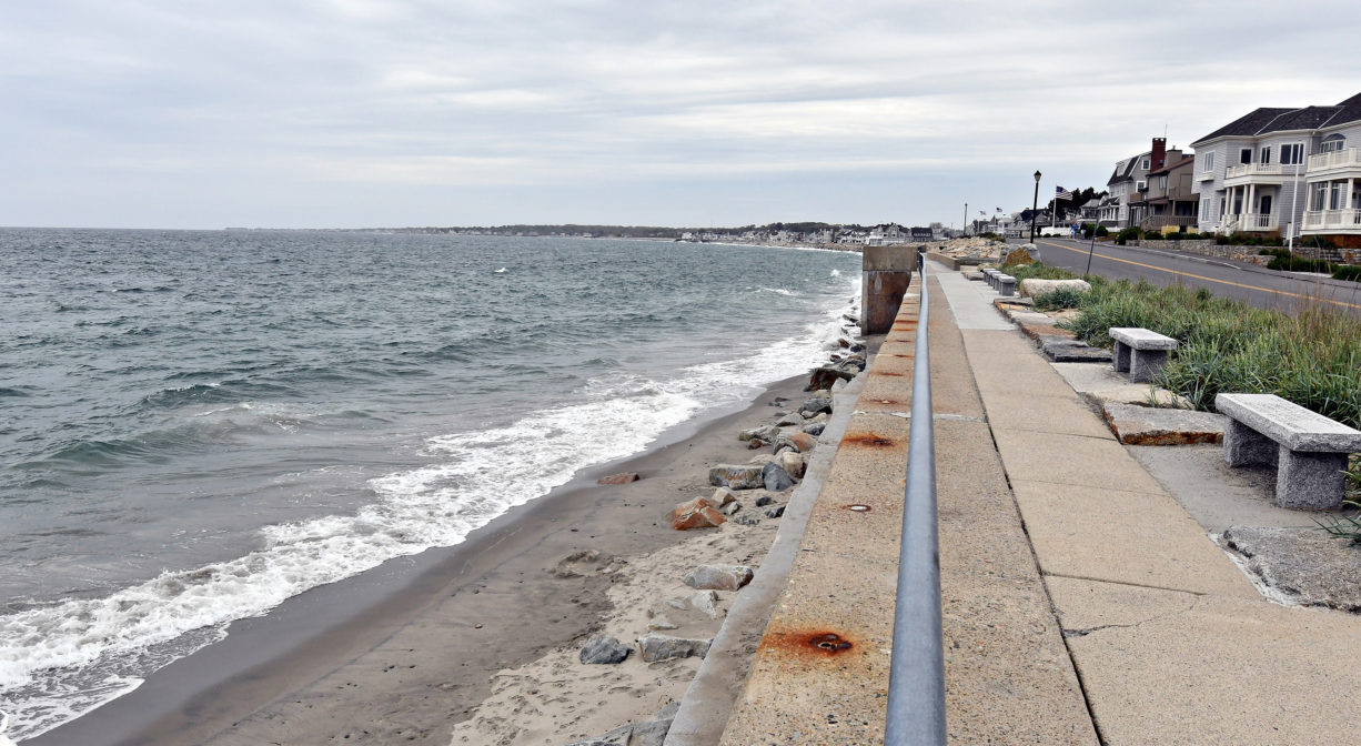A photograph of a sea wall, with benches, overlooking a beach.