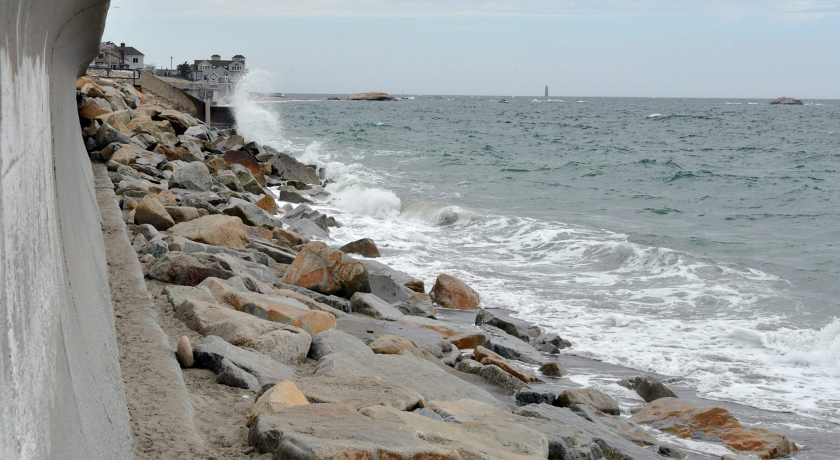 A photograph of a sea wall with large flat rocks between it and the ocean.