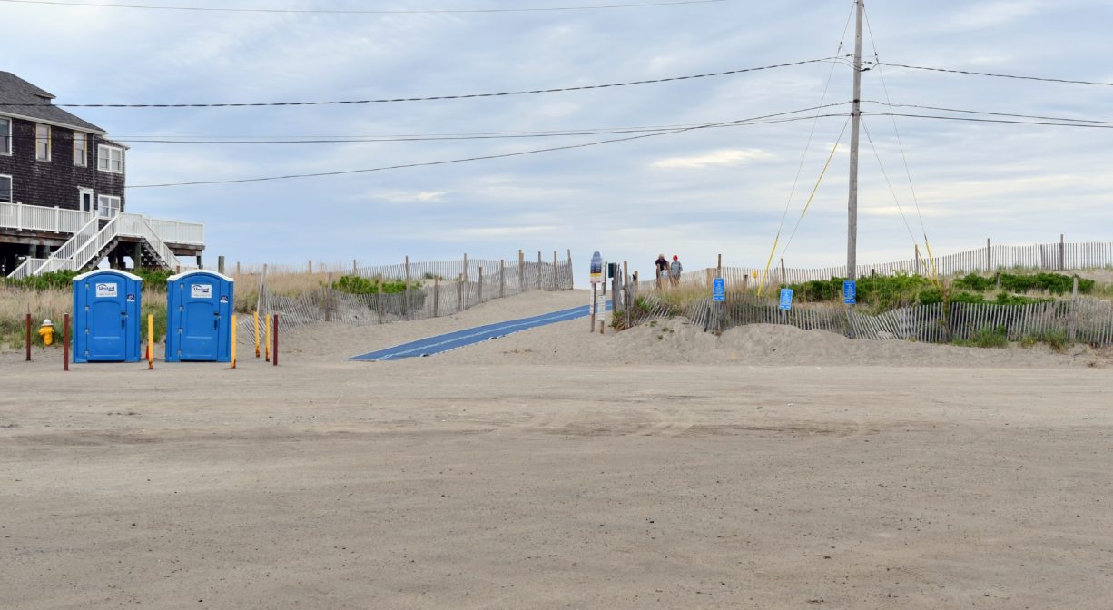 A photograph of the entrance to a beach, with an access mat and porta-potties.