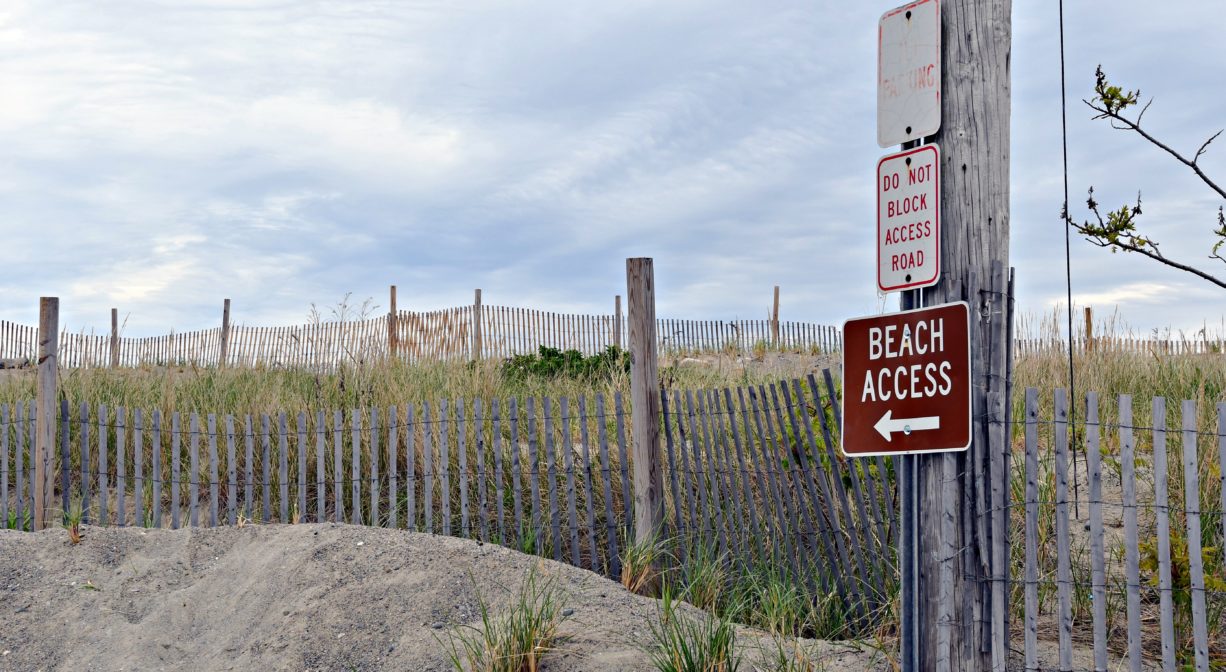 A photograph of a fenced in dune area with some property signs.