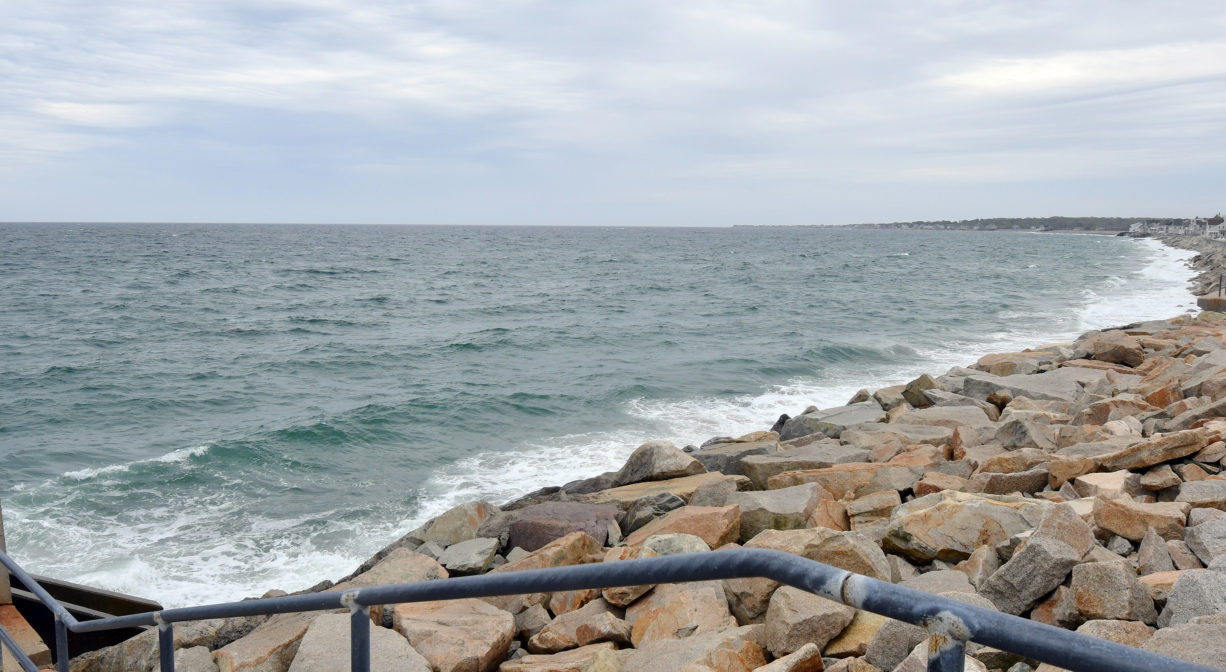 A photograph of a railing leading to a rocky beach.