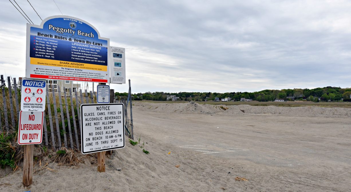 A photograph of the entrance to a beach, with a property sign to one side.