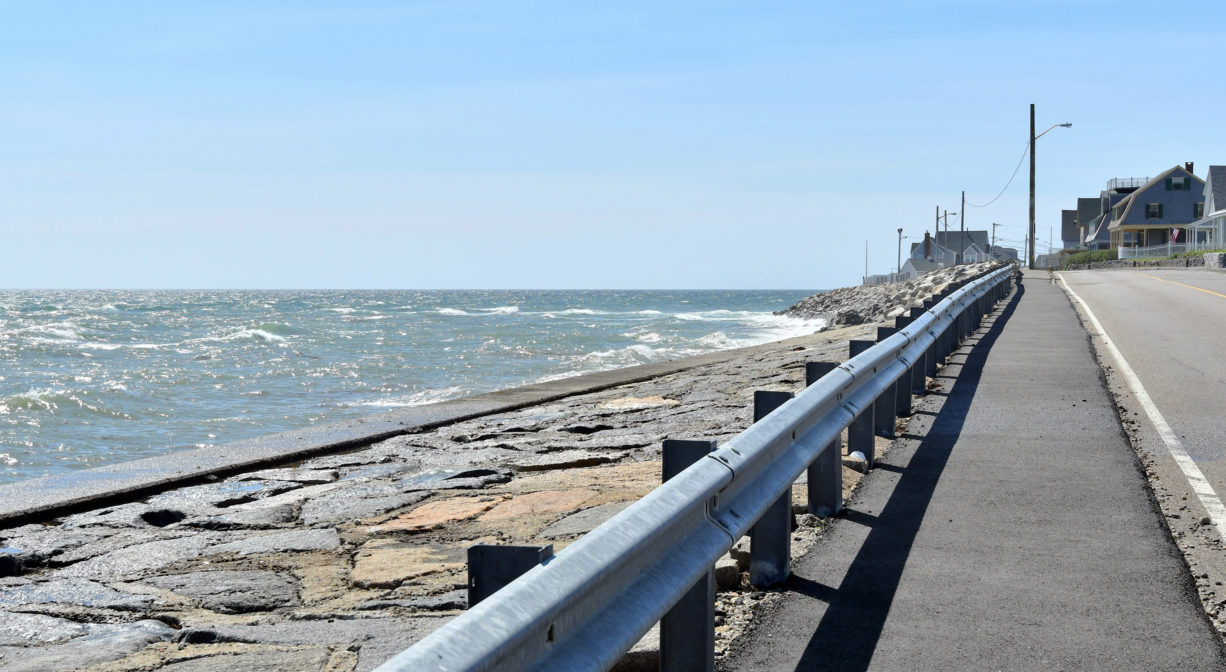 A photograph of a paved walkway beside a seawall.