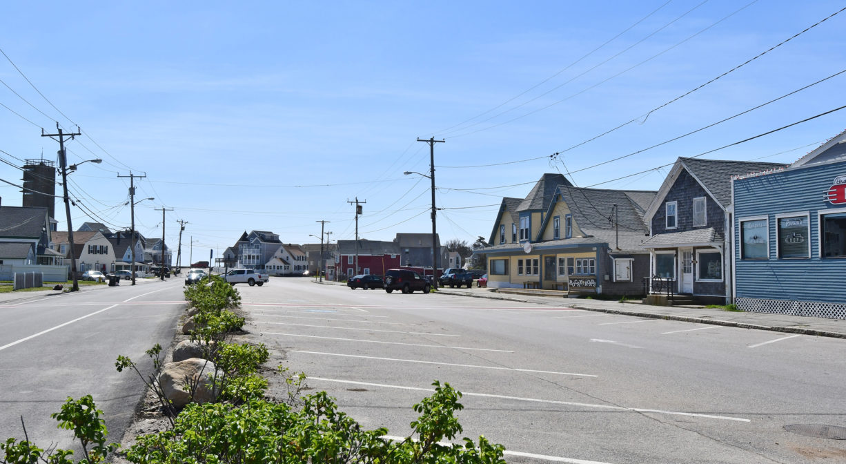 A photograph of a parking area with houses and businesses at its borders.