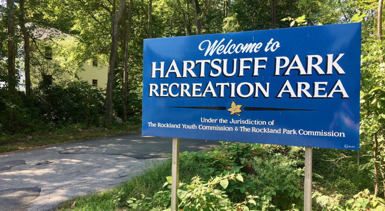 Blue sign for Hartsuff Park Recreation Area with trees and an entrance road in the background.