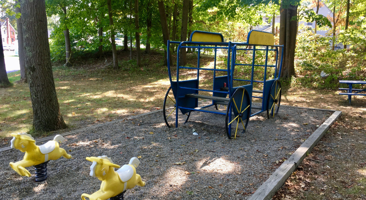 Photograph of outdoor play structures for children with a horse and carriage theme in a wooded setting.