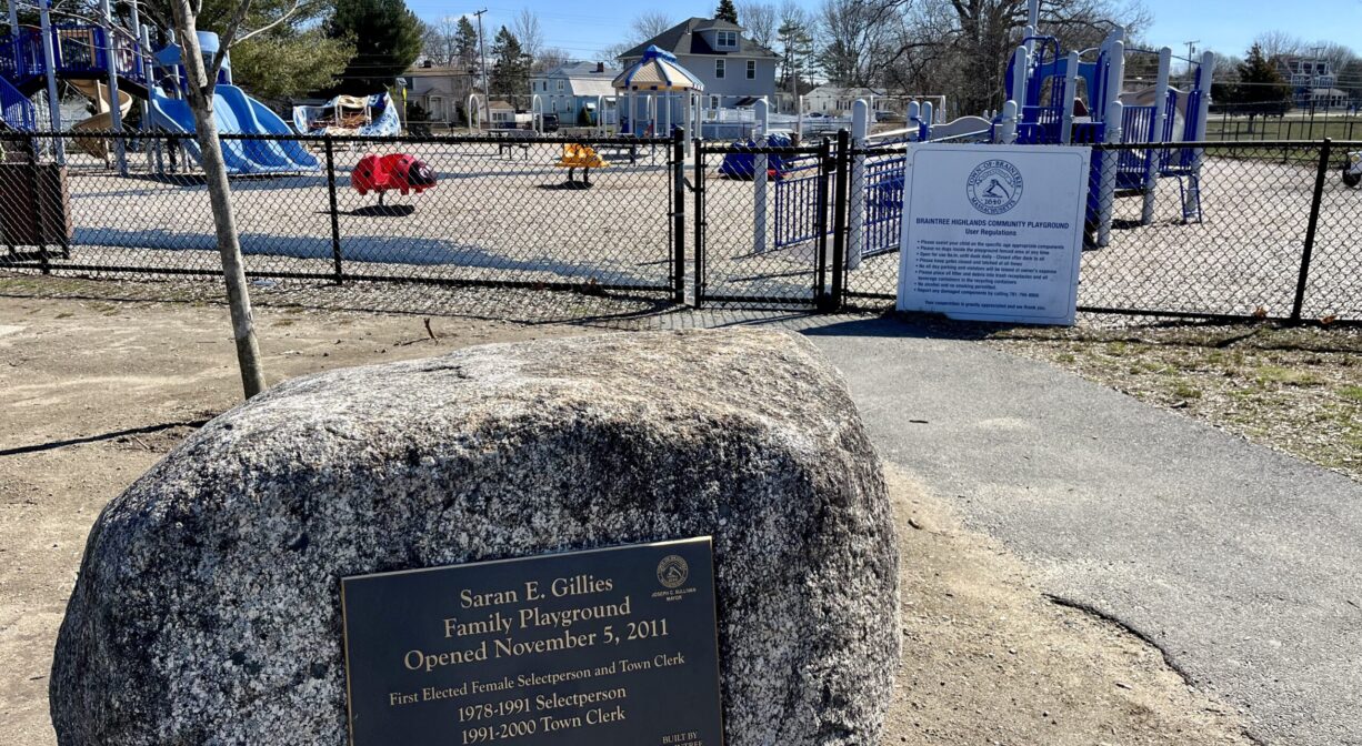 A photograph of a memorial with a playground in the background, plus a paved walkway.