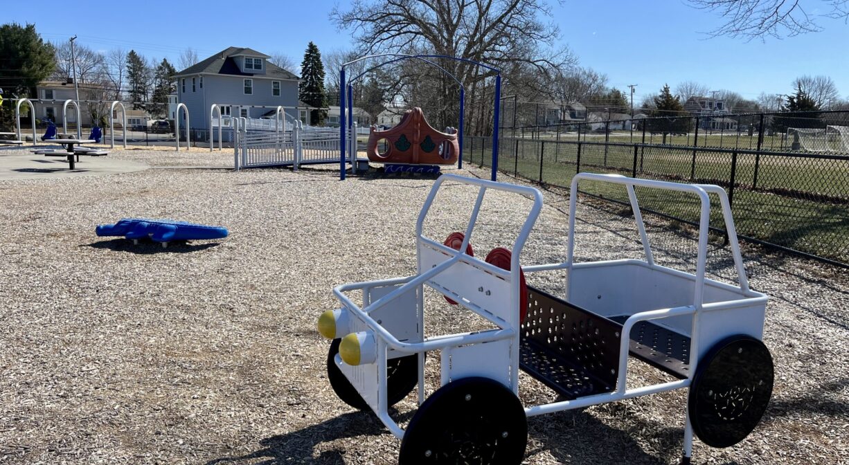A photograph of a play structure shaped like a car, within a playground.
