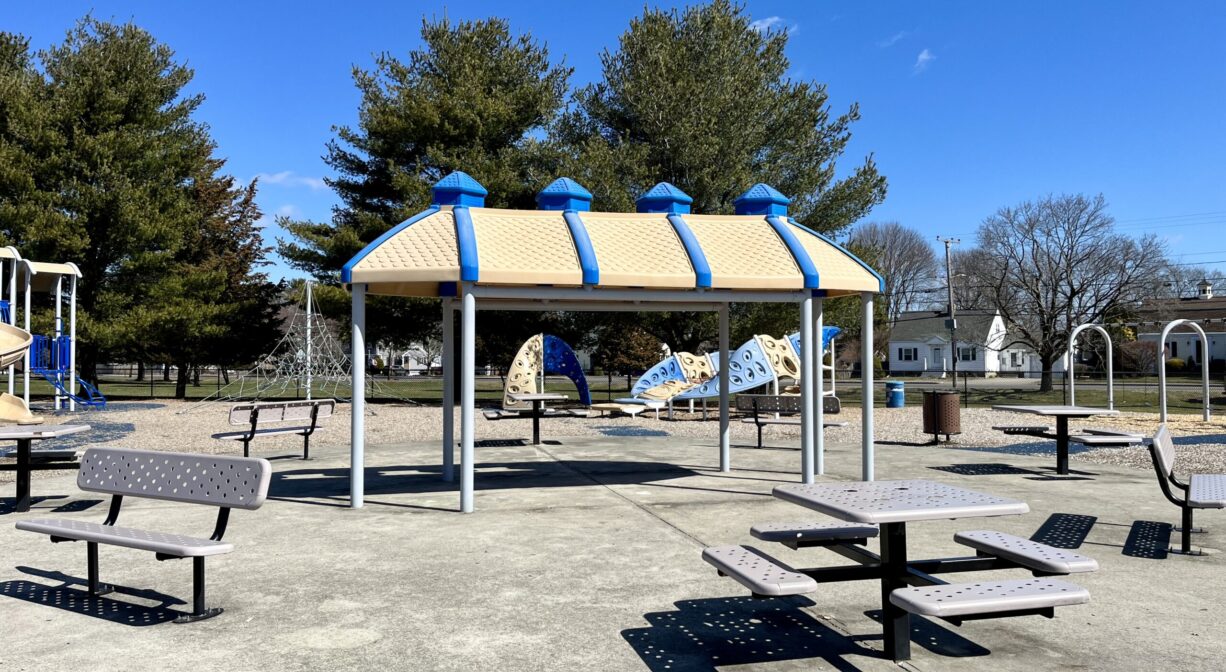 A photograph of picnic tables and a shade structure, within a playground.