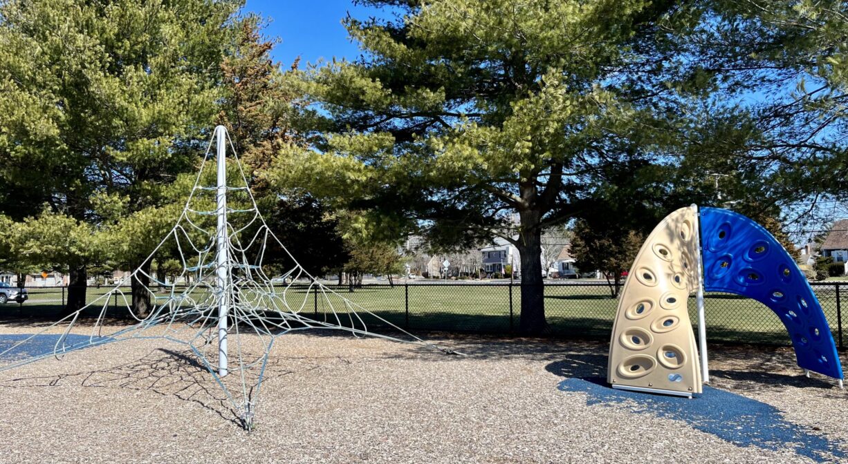 A photograph of a climbing web and a climbing wall within a playground.