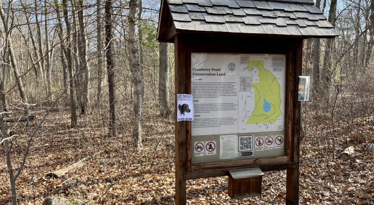 A photograph of an informational kiosk, beside a forest.