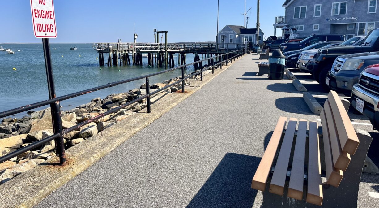 A photograph of bench beside a paved pathway, overlooking a bay.