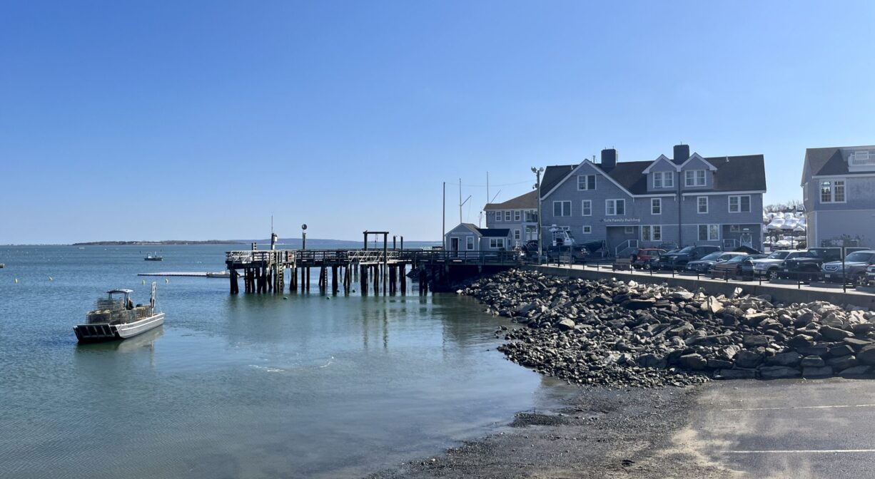 A photograph of a large boat ramp and a pier on a bay with a building in the distance.