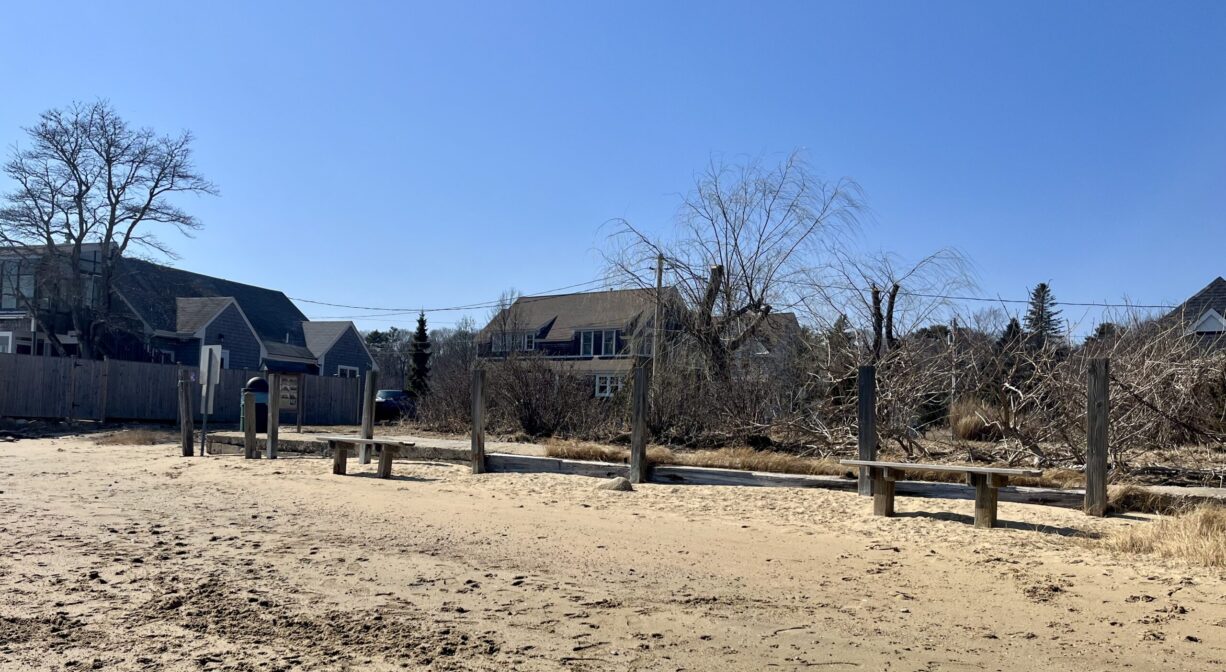 A photograph of a row of benches at the edge of a sandy beach.