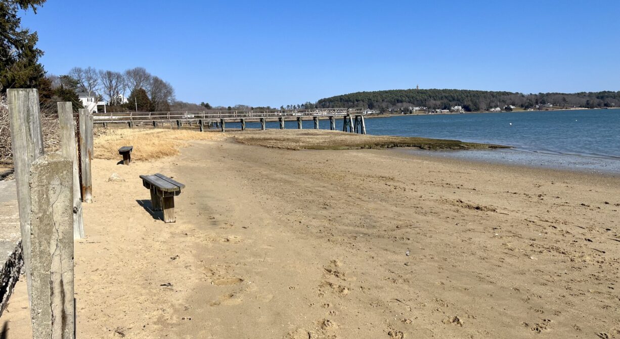 A photograph of a sandy ocean beach at low tide with a row of benches to one side.