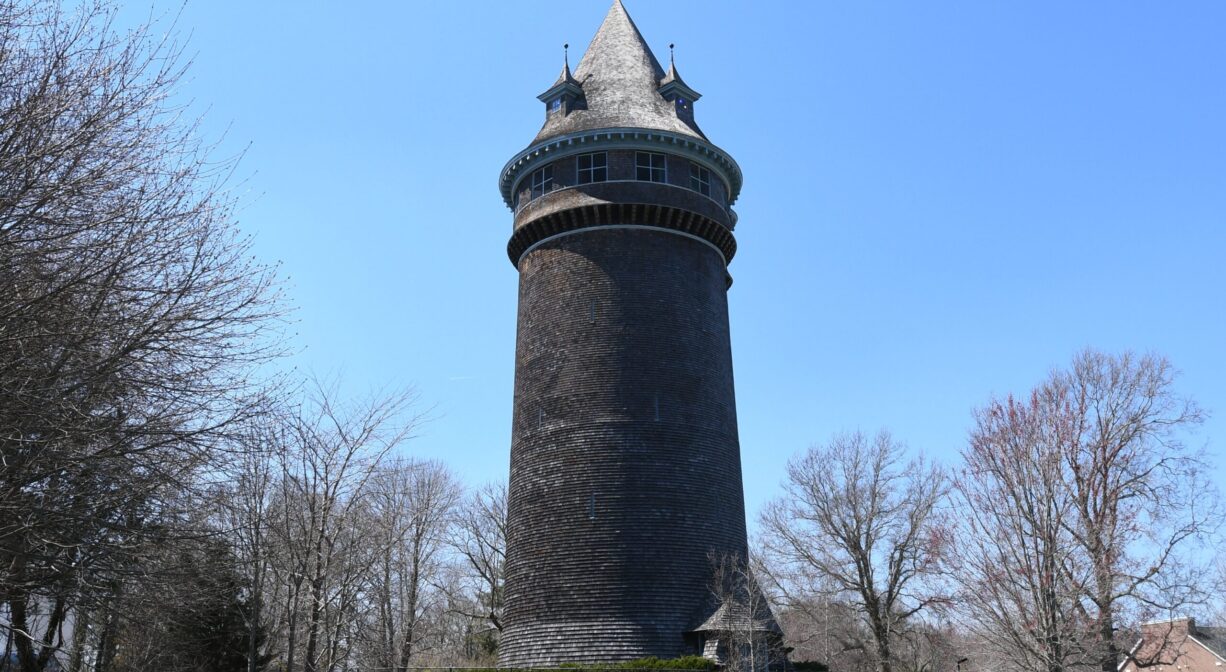 A photograph of an ornate water tower, set on the lawn with blue skies.