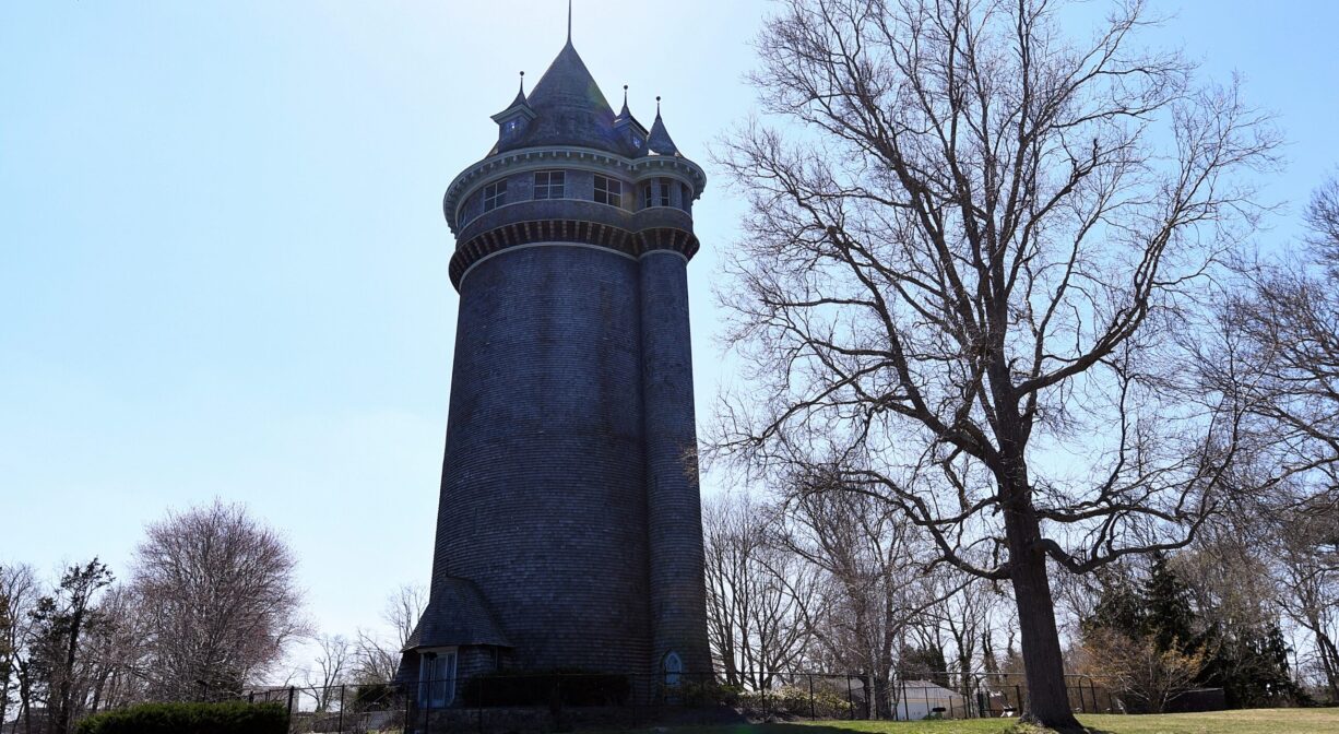 An ornate tower, on a lawn with some trees.