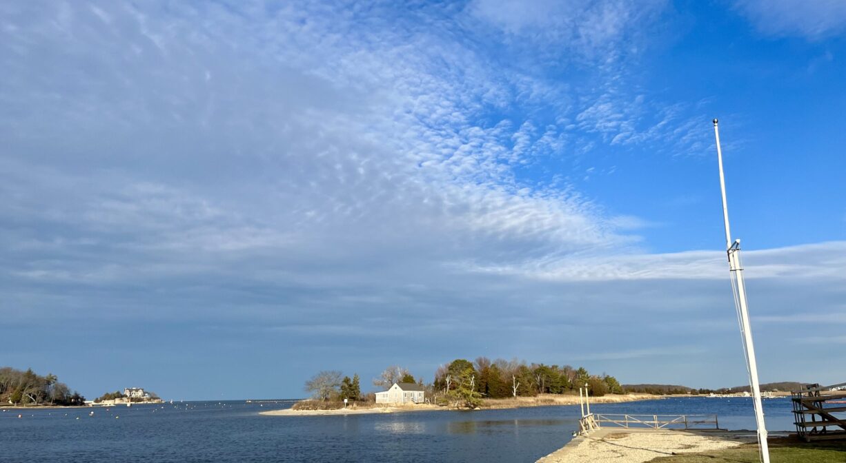 Photograph across the water of a small beach island with a white cottage on it and some trees.