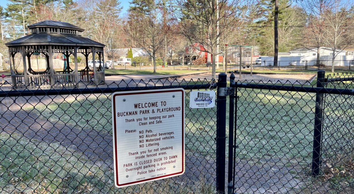 A photograph of an entrance gate to the playground, with a brick path and a gazebo in the background.