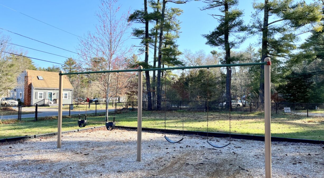 A photograph of a row of swings, within a playground.