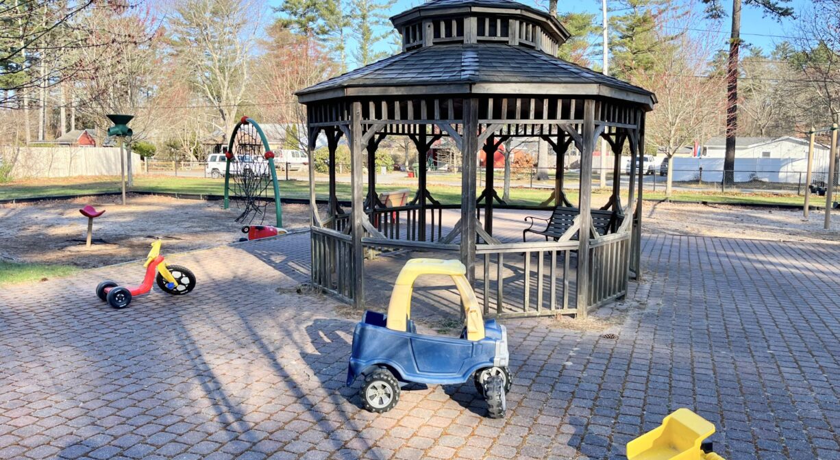 A photograph of a gazebo surrounded by paving stones with scattered riding toys.