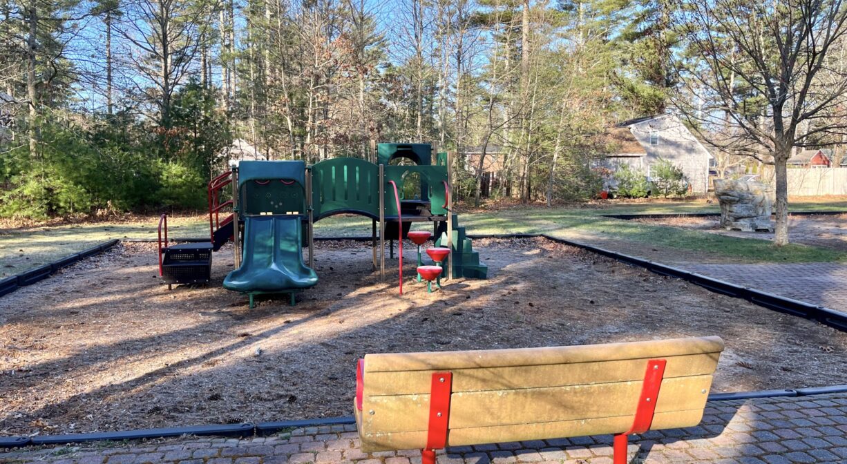 A photograph of a bench beside a play structure, with paving stones underfoot.