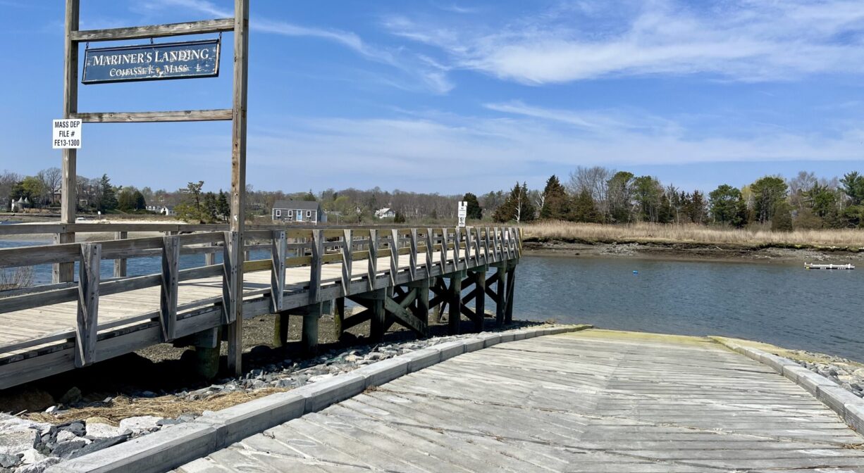A photograph of a concrete launch ramp beside a fishing pier, on a river.