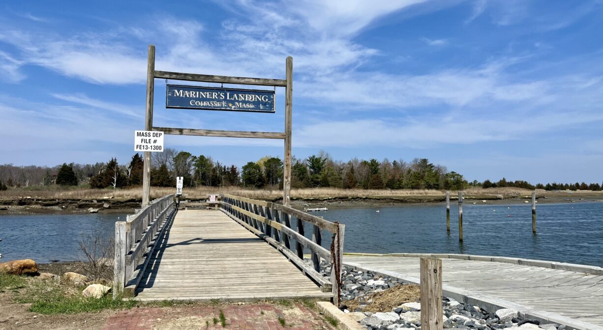 A photograph of a wooden fishing pier on a river, with a brick walkway.