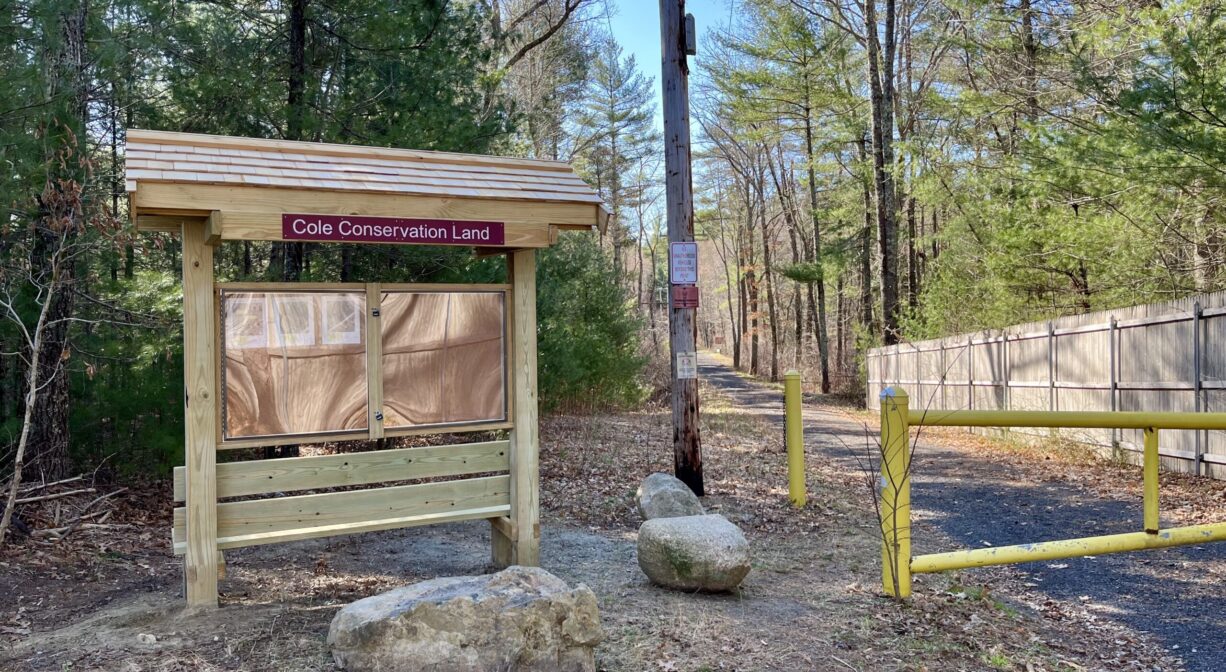 A photograph of an informational kiosk beside a gated trailhead.