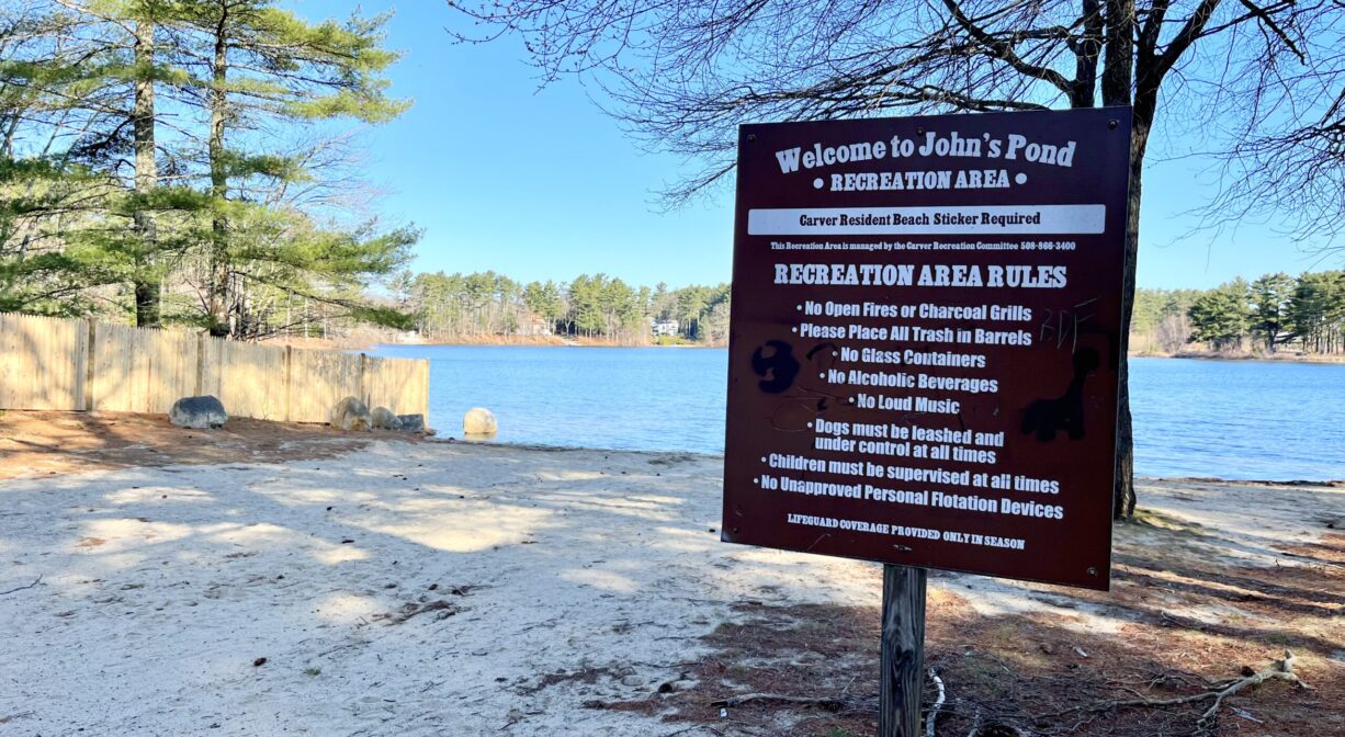 A photograph of a property sign and a beach with a pond in the background.