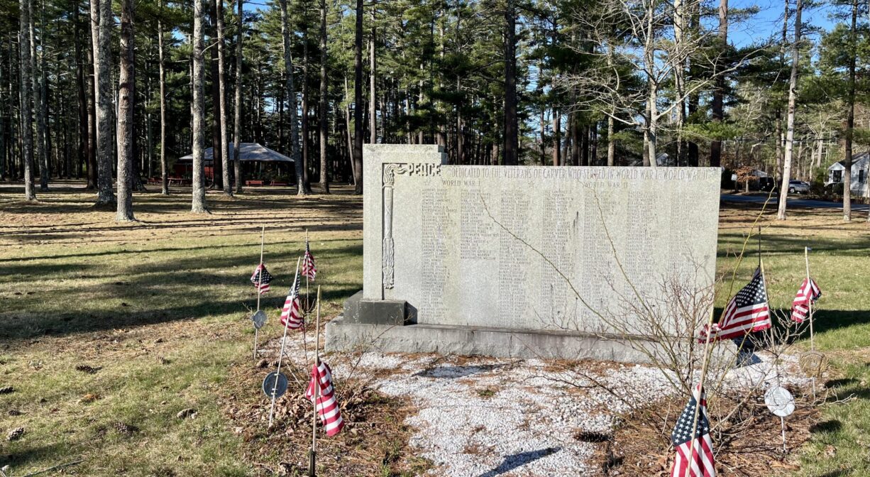 A photograph of a granite war memorial on grass, with trees in the background.