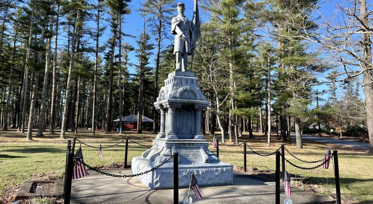 A photograph of a granite war memorial on grass, with trees in the background.