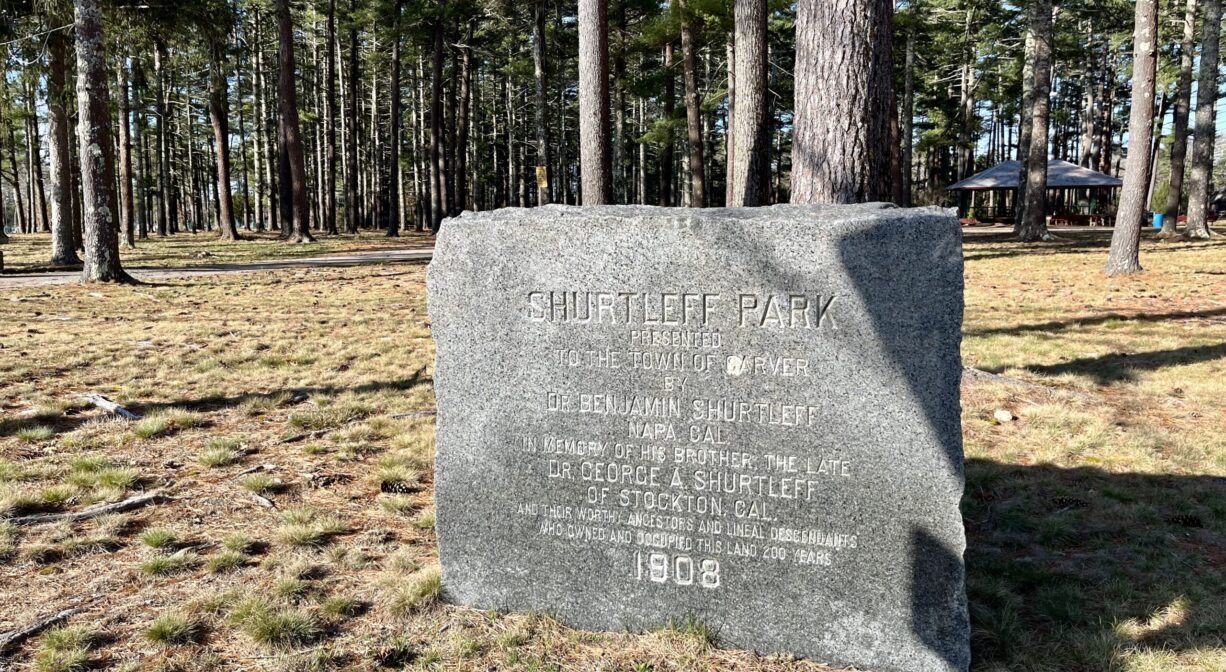 A photograph of a granite property sign, on grass, with trees in the background.