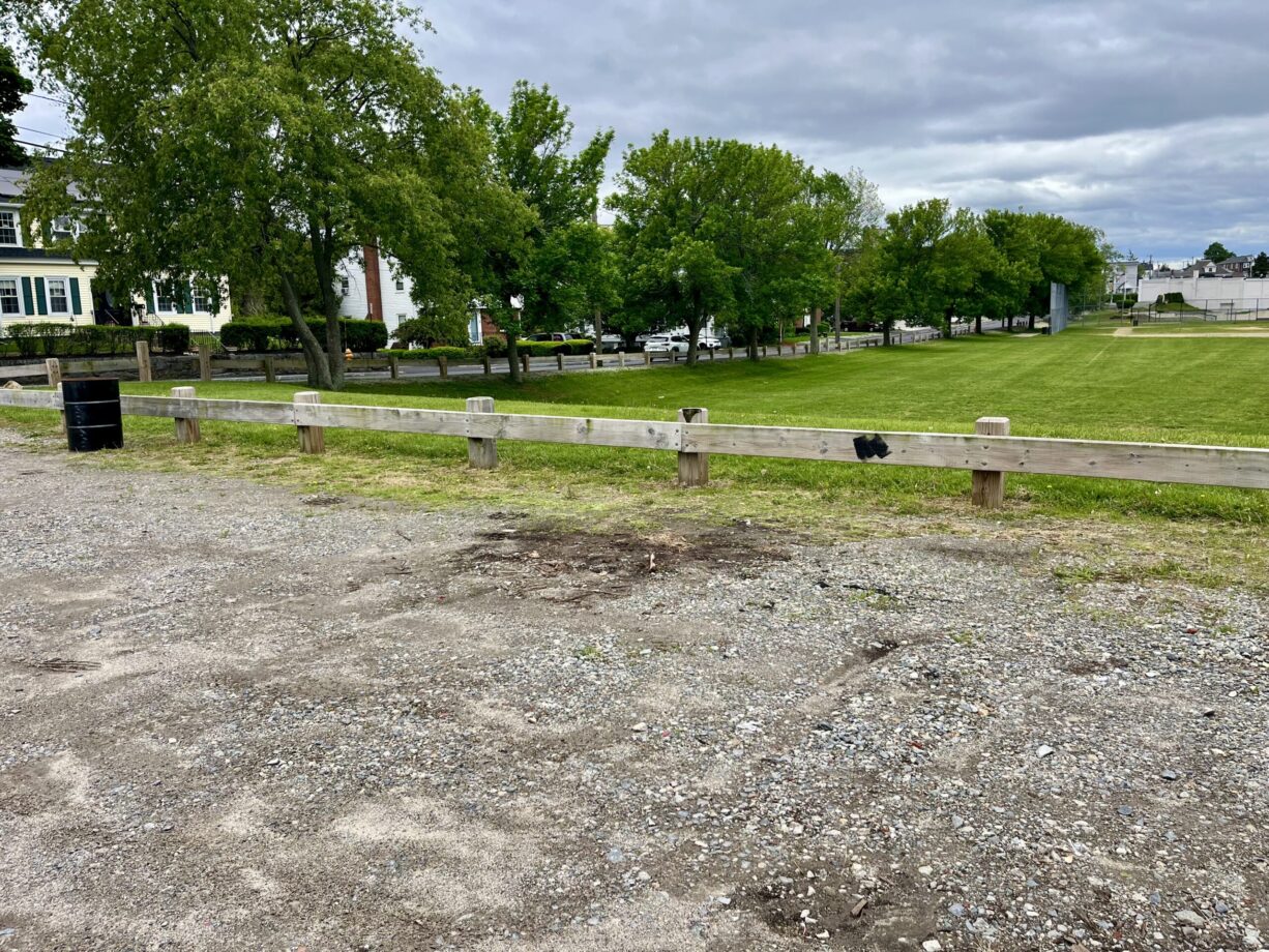 A photograph of an unpaved parking lot beside a park.
